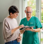 Eine Frau schaut mit einem Pfleger auf ein Tablet.