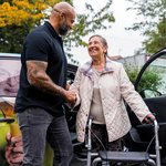 Ein Mitarbeiter des Ambulanten Dienstes begrüßt eine Seniorin, während sie aus dem Fahrdienst aussteigt.