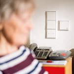 Eine Seniorin im Anschnitt im Hintergrund ein Telefon
