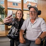 Eine junge Frau macht mit einem Bewohner im Rollstuhl ein Selfie.