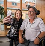 Eine junge Frau macht mit einem Bewohner im Rollstuhl ein Selfie.