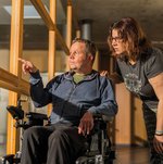 Ein Bewohner im Rollstuhl zeigt einer jungen Frau etwas durch das Fenster.