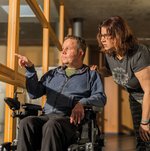 Ein Bewohner im Rollstuhl zeigt einer jungen Frau etwas durch das Fenster.