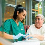 Eine Pflegerin massiert die Hand einer Seniorin